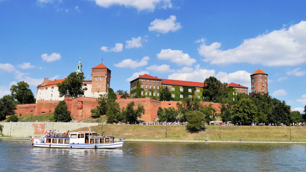 Wzgórze wawelskie z zamkiem królewskim nad Wisłą w Krakowie, bezchmurne letnie niebo, statek spacerowy na rzece.