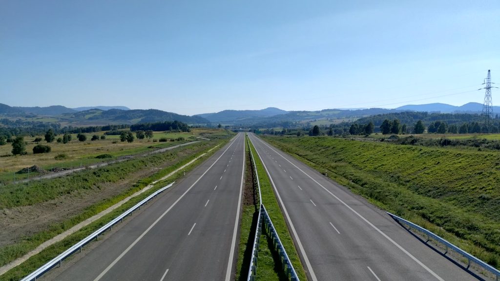 Pusta dwujezdniowa droga ekspresowa S3 z barierami ochronnymi, w tle wzgórza i pola.