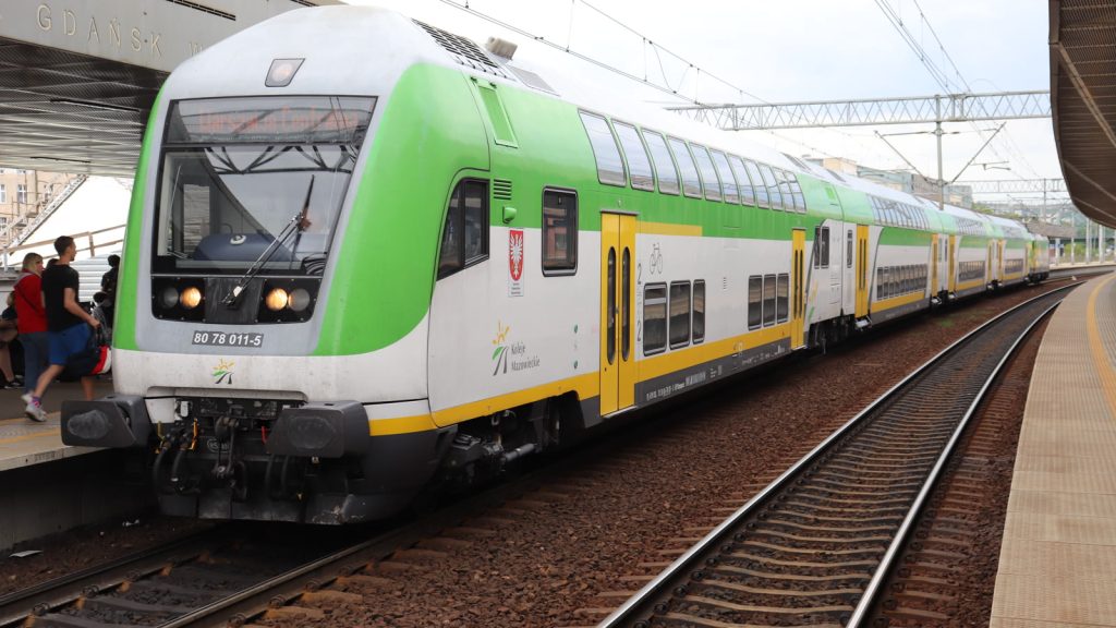 Zielono-biały piętrowy pociąg Kolei Mazowieckich z tablicą kierunkową Warszawa Centralna przy peronie stacji Gdańsk Wrzeszcz, obok wsiadający podróżni.